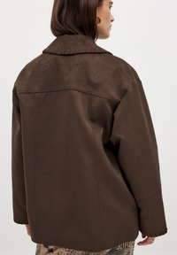 Brown suede jacket with a large collar, loose fit, and stitching details along shoulder seams and cuffs. Suitable for layered outfits.