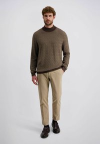 Brauner Pullover mit Muster und runder Halslinie, beigen Hosen und dunkelbraunen Schuhen. Der Pullover hat ein strukturiertes Rautenmuster.