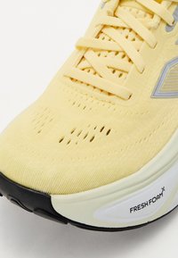 Lys gul idrettssko med en strikket overdel, perforeringer for å gi pusteegenskaper, og en gummisåle i svart og hvitt med "FRESH FOAM" etikett.