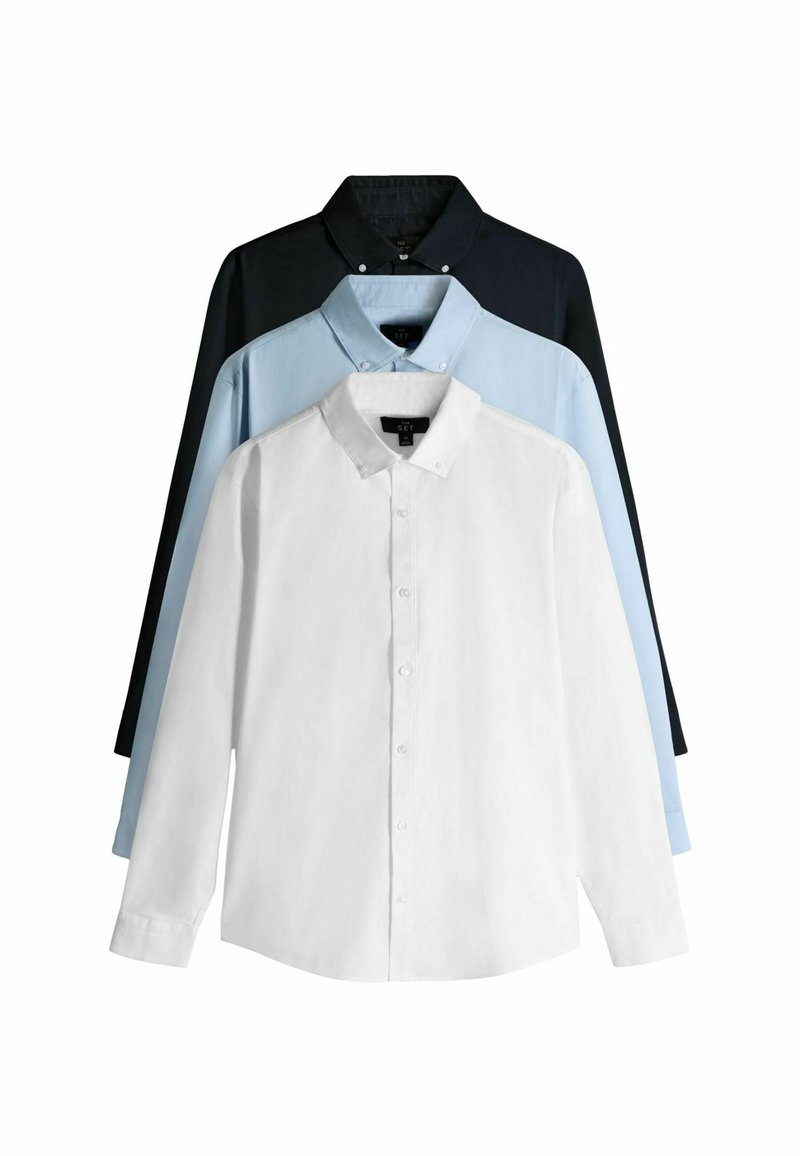 Trīs pogājamo krekla paraugi: priekšā balts krekls, aiz tā gaiši zils krekls un tumši zils krekls aizmugurē. Kokvilnas audums, garas piedurknes.