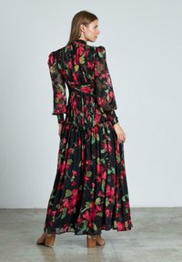 Lang bloemig jurkje met een zwarte achtergrond en rode en groene bloemen, doorschijnend materiaal, gerimpelde taille en lange pofmouwen.