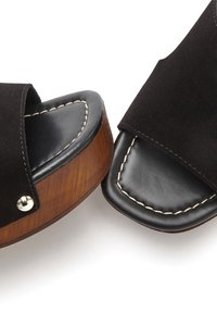 Black suede slide sandals with open toes, leather insoles, wood-grain platform heels, and white stitching accents. Silver hardware detail included.