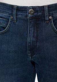 Sötétkék farmernadrág klasszikus szabással, öt zsebes kialakítással, réz varrással és fekete fém patent gombbal a deréknál.
