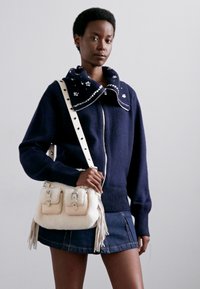 Maglione in lana con zip navy, dotato di colletto testurizzato e dettagli decorativi, abbinato a una borsa color crema con frange e due tasche.