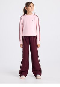 Hellrosa, flauschiger Pullover mit gerippten Bündchen. Locker sitzende, dunkelburgunderfarbene Hose mit weißen Seitenstreifen. Lässiges, sportliches Outfit.