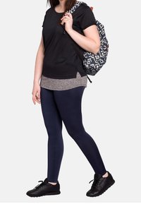 Woman wearing black t-shirt, gray undershirt, navy leggings, black sneakers, carrying a blue and white patterned backpack over one shoulder.