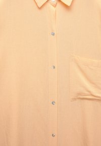 Světle oranžová košile s knoflíkovou přední částí, špičatým límcem, náprsní kapsou a průhlednými knoflíky, vyrobená z hladkého, texturovaného materiálu.