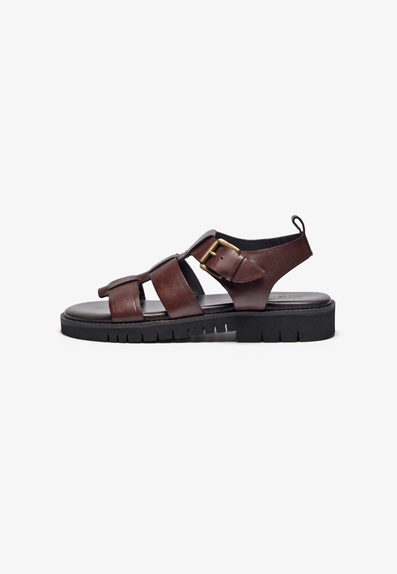 Brune lær sandaler med tre brede stropper, metalspenne, åpen bak, og en tykk svart gummisåle med teksturert mønster.