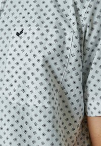 Lichtblauw kortemouwenshirt met een bloemenpatroon in zwart, voorzien van een borstzak en een subtiele v-vormige detail op de zak.