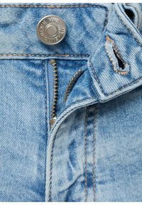 Svetlo modra denim tkanina z vidnim zadrgo in zakovico iz mesinga. Ima obrabljene poudarke in kontrastno šivanje.