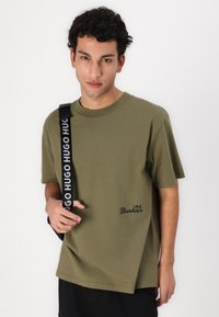 Olivově zelené bavlněné tričko s krátkými rukávy, kulatým výstřihem a zakřiveným lemem. Na dolní přední části je černé logo "Barbour".