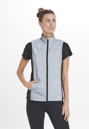 Gilet sans manches gris clair avec un col montant, fermeture éclair à l'avant et manches courtes noires. Doté de poches latérales et d'une texture lisse et légère.