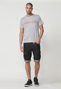 Gray cotton t-shirt with orange graphic print, paired with knee-length black cargo shorts featuring rolled cuffs and side pockets.