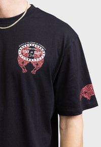 Camiseta de algodón negra con gráficos de tigre rojo en la parte frontal y la mangas, escote redondeado y mangas cortas. Textura suave.