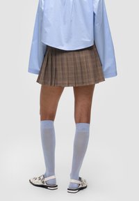 Gonna plettata a quadri marrone con una camicia oversize azzurra. Calze al ginocchio azzurre e sandali argentati con un dettaglio di design.