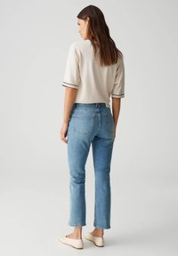 Beige Kurzarmoberteil mit schwarzem Saum, kombiniert mit blauen Jeans im Slim Fit und fransigem Saum. Helle Halbschuhe.