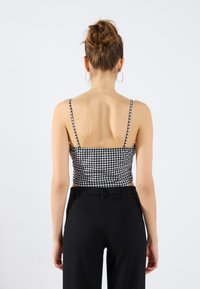 Sort-hvidternet crop top med tynde stropper, tætsiddende design og glat tekstur, parret med skræddersyede sorte vide bukser.