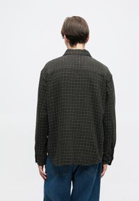 Camisa de flanela xadrez masculina com uma base verde escura, padrão de grelha branca, punhos com botões e um ajuste descontraído. A vista traseira mostra uma textura suave.