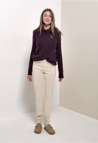 Pull en maille violet, pantalon beige fuselé, chaussures en cuir tan à enfiler, et chaussettes crème ; textures lisses avec une coupe décontractée.
