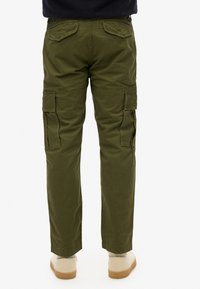 Cargo bukser i armygrøn bomuld, med sidelommer, baglommer og en lige ben-design. Båret med beige fodtøj.