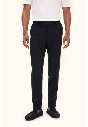 Pantalons tailleur bleu marine en tissu à la texture lisse, avec une taille standard et une coupe ajustée, associés à des mocassins foncés.