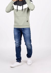 Felpa con cappuccio verde chiaro con motivo chevron nero e bianco, tasca a marsupio, abbinata a jeans blu strappati e sneakers bianche.