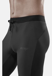 Zwarte compressie legging met een tailleband met trekkoord, een gladde textuur en een logo aan de linkerzijde, met een aansluitend ontwerp en rekbaar materiaal.