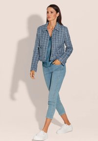 Blauwe krijtstreepjack met een gestructureerde stof, cropped ontwerp en knopen aan de voorkant, gecombineerd met lichtblauwe denim broek met versieringen en witte sneakers.