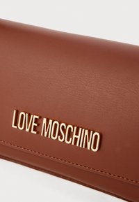 Barna szintetikus bőrből készült pénztárca arany "LOVE MOSCHINO" logóval, sima felülettel és varrott részletekkel a tartósság érdekében. Egyszerű, téglalap alakú design.