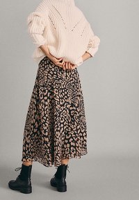 Gebreid crèmekleurig sweater met brede mouwen, gedragen met een vloeiende zwarte rok met een tan luipaardprint, gestyled met zwarte enkellaarsjes.