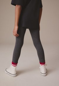 Leggings grises con un diseño ajustado, combinados con zapatillas blancas de caña alta y calcetines a rayas en rojo y rosa, sobre un fondo neutro.