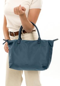 Tamsiai mėlynas maišelis su dviem rankenomis, pagamintas iš lygaus, tvirto materialo. Turi dvigubas rankenas ir užtrauktuką, subtilūs siuvimo akcentai.