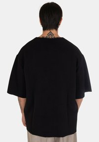 Pullover nero con una vestibilità ampia, texture a coste, spalle scese e scollatura ampia, con un orlo arrotondato sul retro.