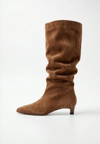 Hnědá semišová bota do půli lýtka s volným sárem, špičatou špičkou a nízkým podpatkem typu kitten na bílém pozadí.