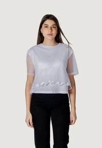 Top corto blanco con mangas transparentes, que presenta un texto bordado a lo largo del dobladillo. Fabricado con tela ligera de textura suave.