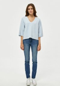 Top azzurro chiaro a maniche corte con scollo a V, realizzato in materiale morbido, abbinato a jeans blu a gamba dritta e sneakers bianche. Stile semplice e fit rilassato.