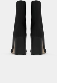 Paire de bottines noires à talons carrés vues de dos sur un fond blanc.