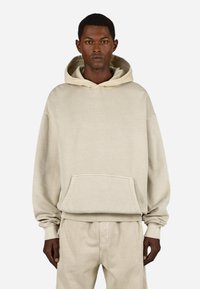 Μπεζ φούτερ με κουκούλα, διαθέτει μπροστινή τσέπη, ριμπ μανσέτες και στρίφωμα. Μαλακή υφή και άνετη εφαρμογή; η επωνυμία είναι διακριτικά κεντημένη στο στήθος.