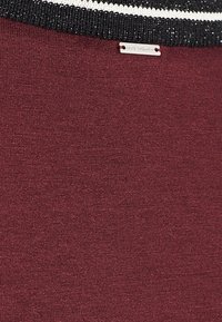 Burgundy sweater with a textured knit, featuring a black and white striped collar and a small metal tag labeled "IXXS WOMEN."