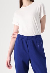 Vit t-shirt med kort ärm som matchas med blåa mjukisbyxor med midjeband och en diskret vertikal logotyp. Mjuk bomullsmaterial.