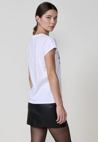 T-shirt blanca con mangas enrolladas, combinada con una mini falda de cuero negra con un patrón texturizado de cocodrilo. Diseño minimalista, colores sólidos.