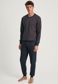 Navy-gepatroniseerde sweatshirt met aansluitende manchetten en bijpassende navy broek. De sweatshirt heeft een geometrisch ontwerp in rood en wit.