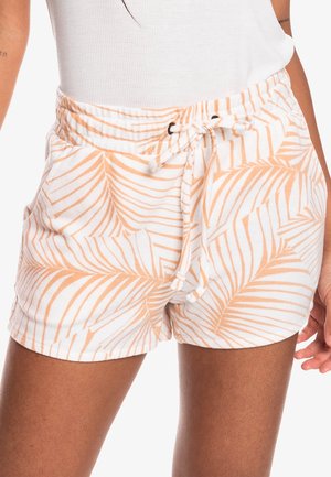 Weiße Shorts mit hellorangefarbenem Palmenblättermuster und Kordelzugbund, getragen zu einem weißen ärmellosen Oberteil an einer Person.