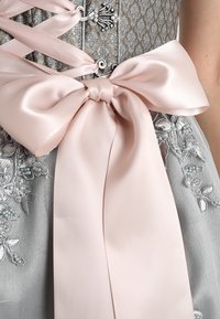 Srebrna sukienka z misternym haftem i koralikami, z dużą różową satynową kokardą w talii oraz dekoracyjnymi elementami sznurowania.