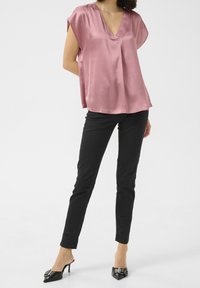 Haut en satin rose avec col en V et manches courtes, associé à un pantalon ajusté noir et des mules noires à talons ornées d'une boucle décorative.