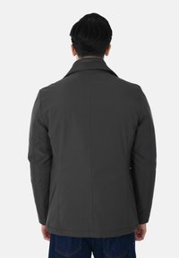 Cappotto grigio scuro su misura con colletto a rever e design senza cuciture. Tessuto liscio con silhouette aderente, che mette in mostra uno stile minimalista.