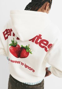 Krémová mikina s grafickým motívom dvoch jahôd a červeným textom "Berry Sweet" a "tak sladké, že sa nedá ignorovať." Mäkká tkanina, voľný strih.