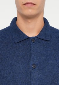 Camisa de mistura de lã azul marinho com colarinho dobrado, dois botões pretos na frente e um acabamento suave e texturizado.