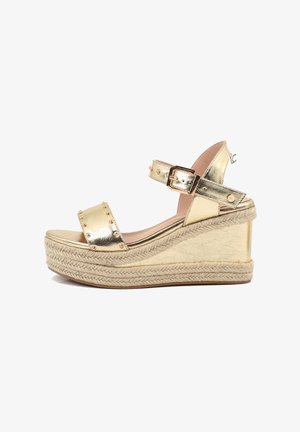 Sandalia tipo cuña metálica dorada con adornos de tachuelas, punta abierta, correa ajustable en el tobillo y plataforma trenzada de yute.