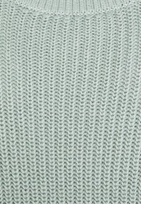 Tissu tricoté vert clair avec un motif texturé de lignes verticales et de motifs en zigzags, fabriqué en fil doux pour une sensation confortable.